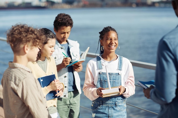 Foto vielfältige gruppe von kindern, die glücklich lächeln, während sie den unterricht im freien im sonnenlicht genießen