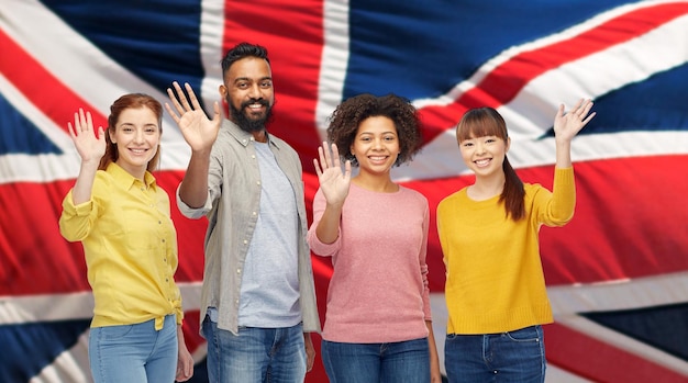 Foto vielfalt, einwanderung und menschenkonzept – internationale gruppe glücklich lächelnder männer und frauen, die vor dem hintergrund der britischen flagge die hände schwenken