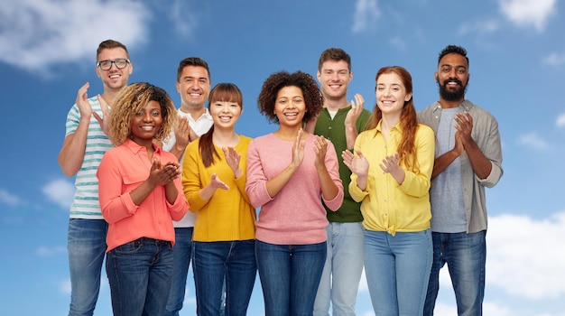 Vielfalt, Rasse, Ethnie und Menschenkonzept - internationale Gruppe glücklicher lächelnder Männer und Frauen über blauem Himmel und Wolkenhintergrund