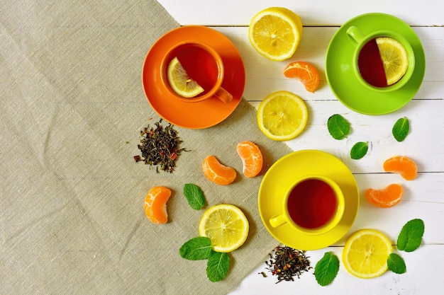 Vielfarbige Tassen mit Tee, Zitronenminze und Mandarine auf weißem Holzgrund