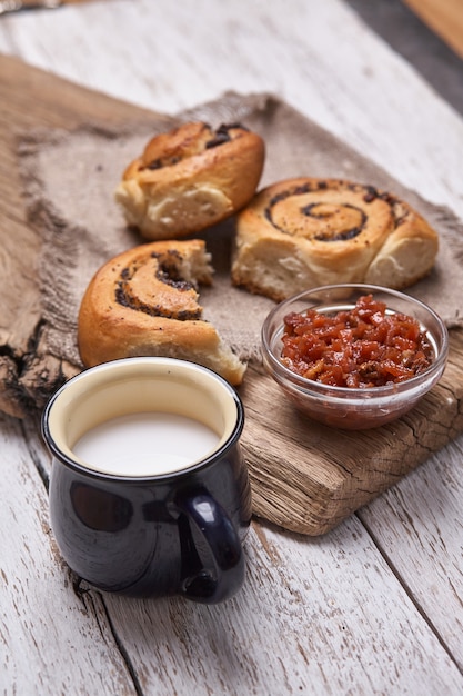 Vielzahl von hausgemachten Blätterteigbrötchen Zimt serviert mit Milchbecher, Marmelade, Butter als Frühstück über weißen Planke Holztisch. Flache Lage, Platz