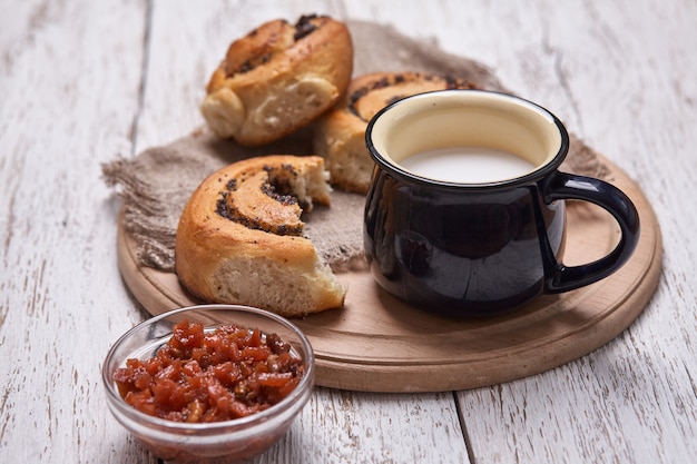 Vielzahl von hausgemachten Blätterteigbrötchen Zimt serviert mit Milchbecher, Marmelade, Butter als Frühstück über weißen Planke Holztisch. Flache Lage, Platz