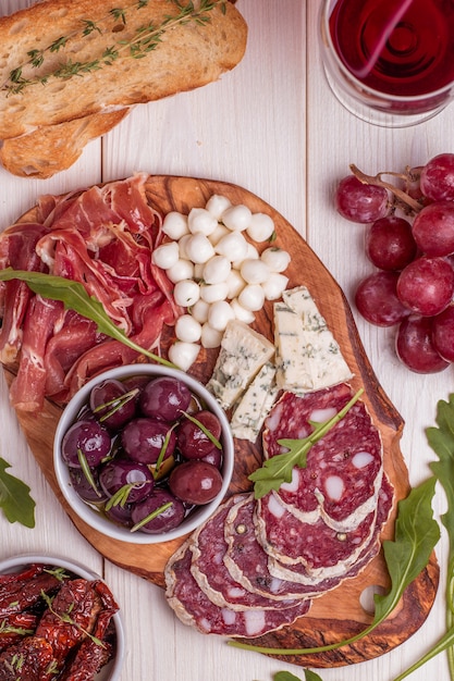 Vielzahl von Käse und Fleisch, Oliven, Trauben, Rucola auf weißem Tisch