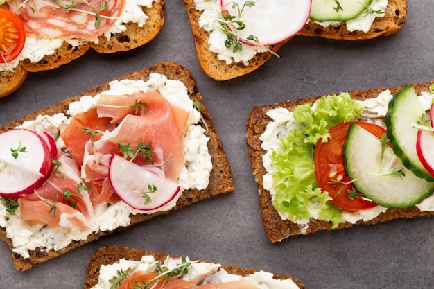 Vielzahl von Mini-Sandwiches mit Frischkäse, Gemüse und Salami.