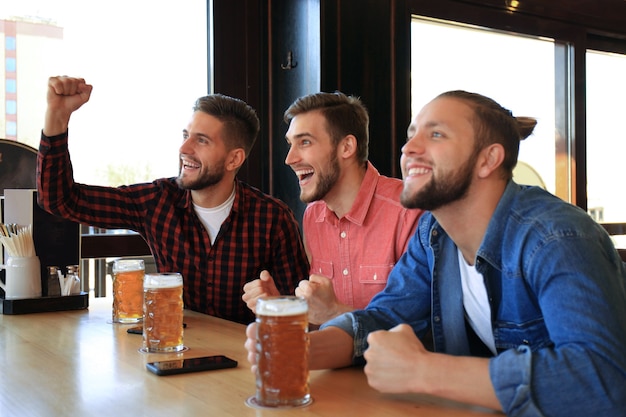 Viendo fútbol en el bar. Amigos felices bebiendo cerveza y animando a su equipo favorito, celebrando la victoria.