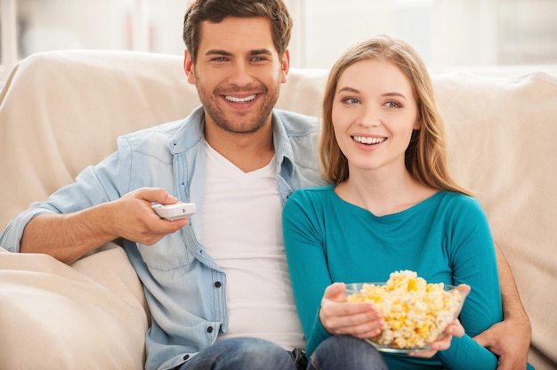 Viendo televisión juntos. Hermosa joven pareja sentada en el sofá juntos y viendo la televisión