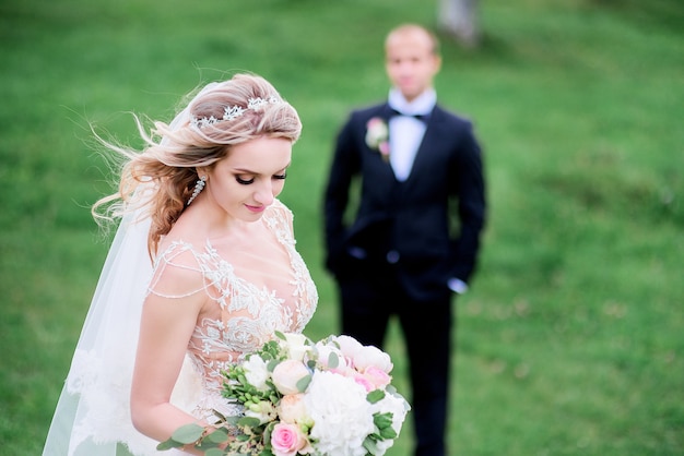 El viento sopla el cabello de la novia mientras ella se para en el césped verde antes de que su novio