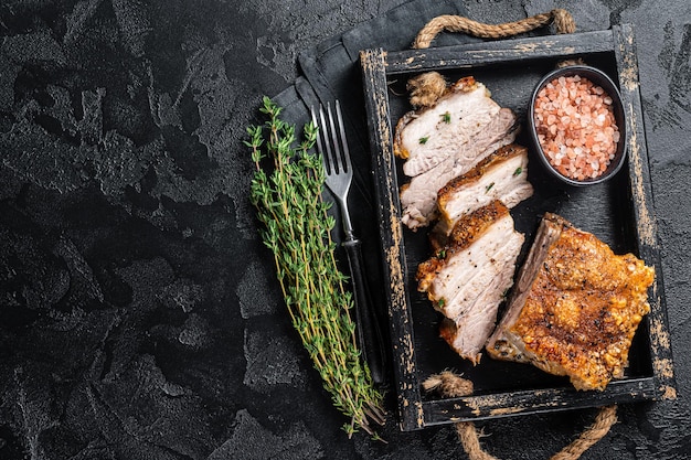 Vientre de cerdo asado crujiente Carne asada en rodajas con corteza en una bandeja con especias Fondo negro Vista superior Espacio de copia