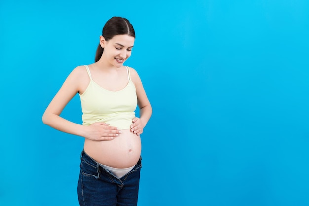 Vientre embarazado en colores de fondo con espacio de copia Futura madre en jeans abiertos está abrazando su panza desnuda Concepto de maternidad