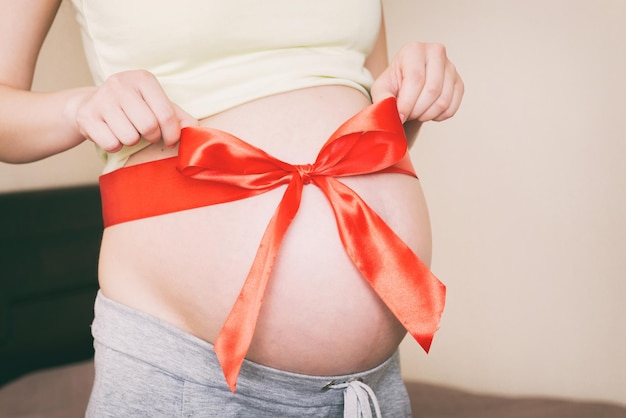 Vientre de una mujer embarazada atada con un lazo rojo sobre un fondo de casa