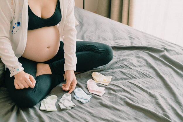 Vientre de mujer embarazada con manos elegir calcetines de bebé