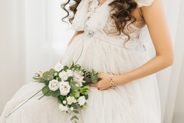 Vientre de una niña embarazada con un hermoso vestido blanco