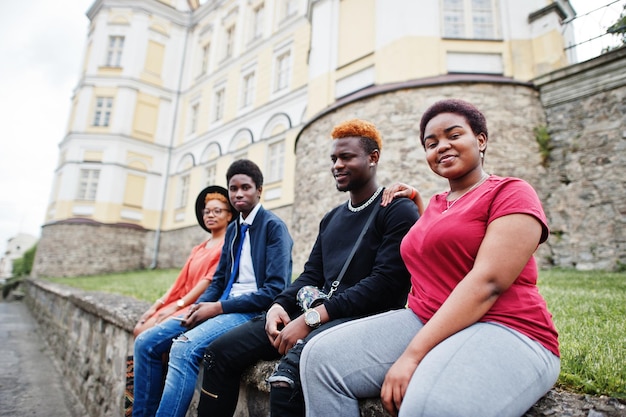 Vier afrikanische Freunde, die sich im Freien amüsieren. Zwei schwarze Mädchen mit Jungs sitzen in einer alten Stadt.