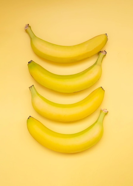 Vier Bananen liegen auf einem vertikalen Schuss der Draufsicht des gelben Hintergrundes