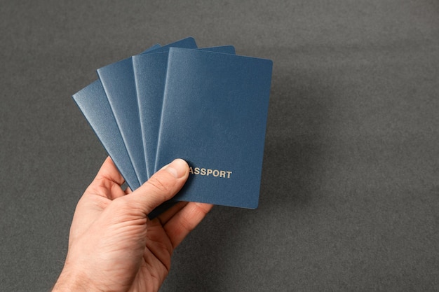 Vier blaue Pässe mit Blankohüllen in der Hand eines Mannes auf schwarzem Hintergrund, offizielles Dokument für Auslandsreisen, Kopierraum-Attrappe
