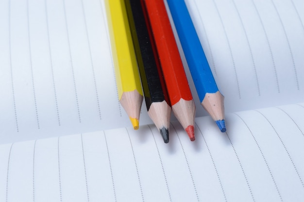 Vier bunte Bleistifte - blau, rot, gelb, schwarz. auf einem offenen Notizbuch liegen.