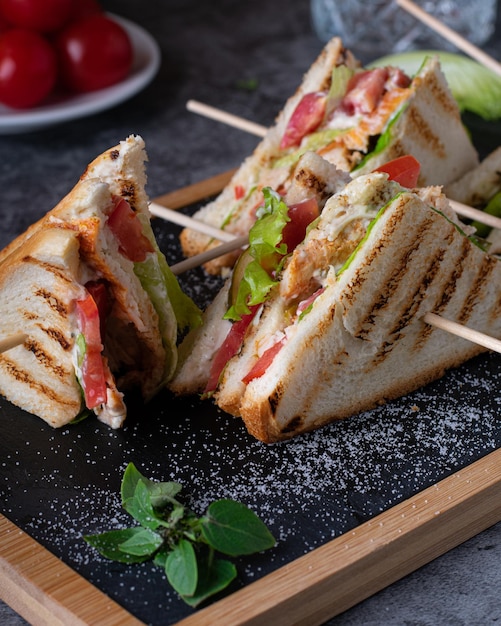 Vier Club-Sandwiches mit Salatkirschtomaten und Käse auf dem Brett vertikal