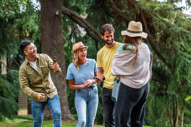 Vier Freunde genießen einen sonnigen Tag im Park, lachen und teilen sich Bier aus einer Tasche, die einer von ihnen mitgebracht hat.