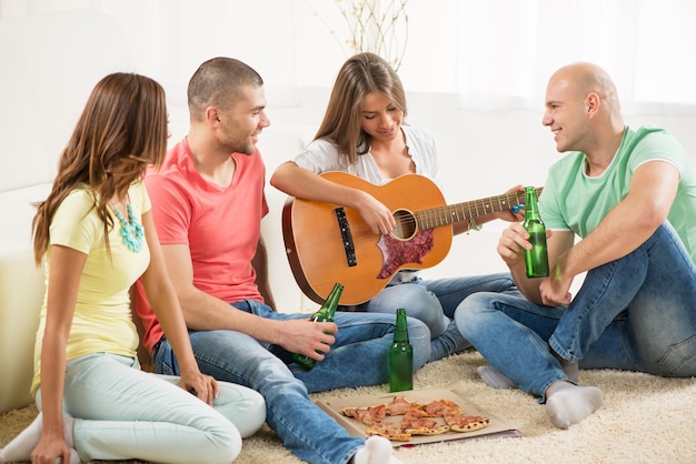 Vier Freunde genießen gemeinsam die Homeparty mit Gitarre und Bier.