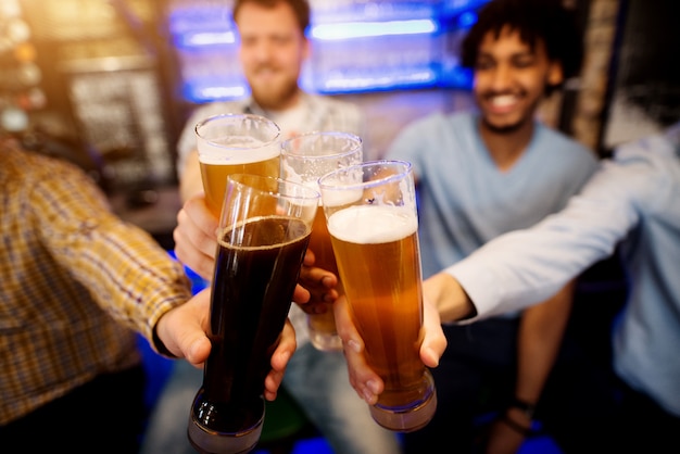 Vier Freunde klirren mit Gläsern Bier in der Kneipe.