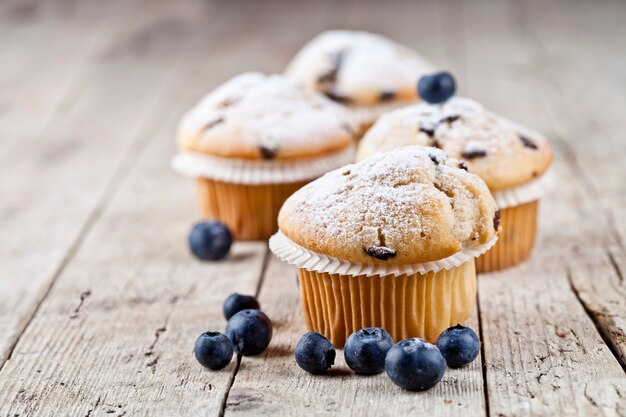 Vier frische selbst gemachte Muffins mit Blaubeeren auf rustikalem Holztisch.