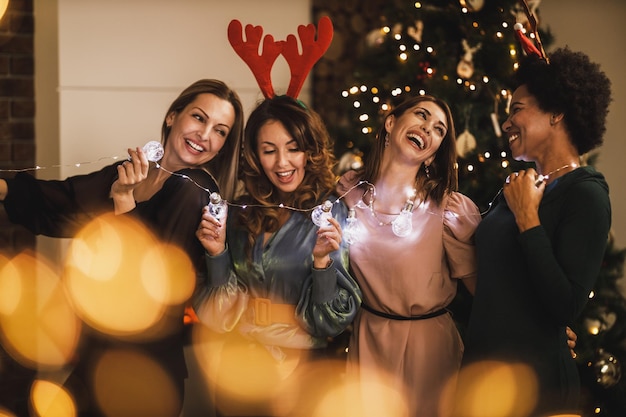 Vier fröhliche multiethnische Mädchen, die sich während der Weihnachts- oder Neujahrsparty mit Glühbirnen amüsieren.