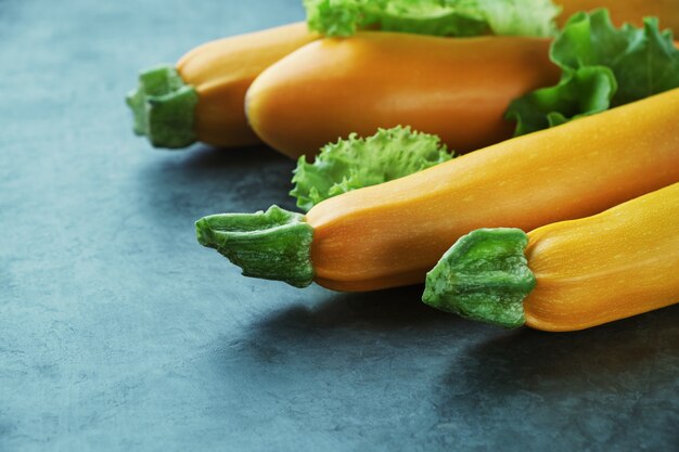 Vier gelbe Zucchini und Salat auf Küchentisch. Ganze rohe Zucchini