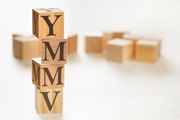 Vier gestapelte Holzwürfel mit den Buchstaben YMMV (bedeutet, dass Ihr Kilometerstand variieren kann) darauf, Platz für Text / Bild in der unteren rechten Ecke
