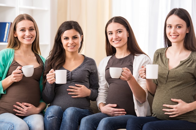 vier glückliche schwangere Frauen mit einer Tasse Tee.