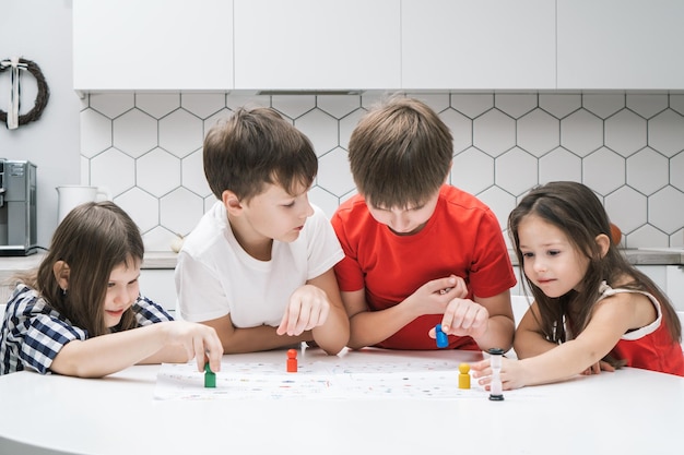 Vier glückselig lächelnde Kinder, die Brettspiele spielen und bunte Figuren auf dem Tisch in der Küche auswählen Entwicklung von Kindern