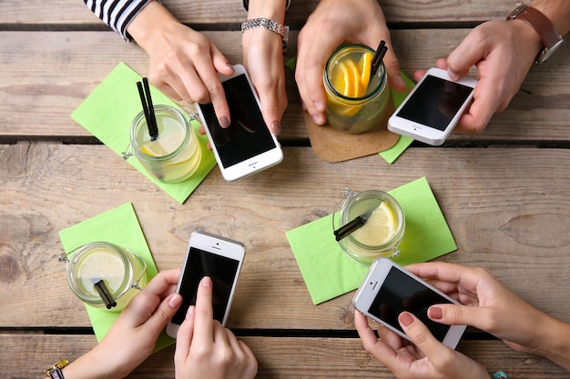 Vier Hände mit Smartphones halten Cocktails auf dem hölzernen Tischhintergrund