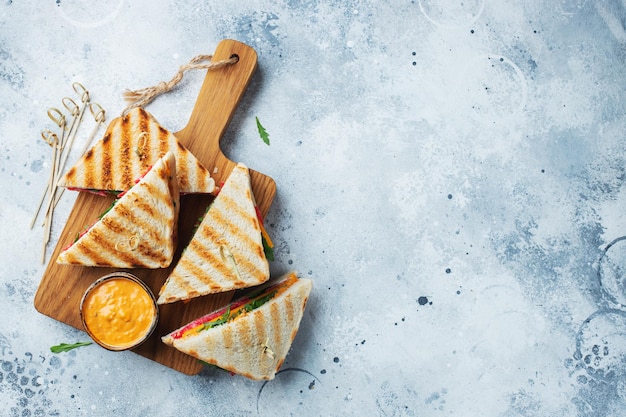 Vier hausgemachte Sandwiches mit Wurstkäse und Rucola auf hellem Betonhintergrund