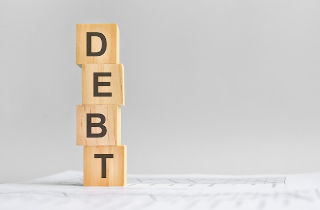 Vier Holzwürfel mit dem Wort DEBT auf dem Hintergrund weißer Jahresabschlüsse, starkes Geschäftskonzept. grauer Hintergrund