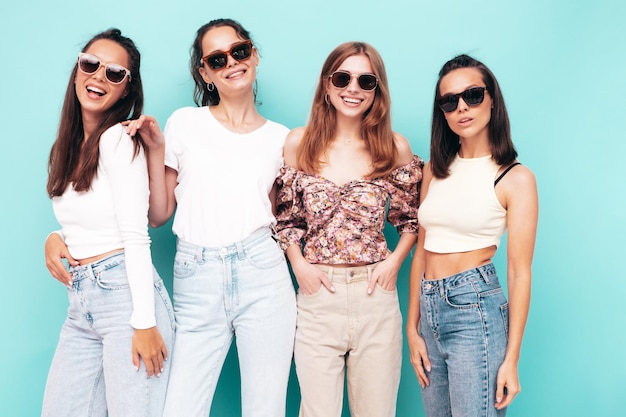 Vier junge, schöne, lächelnde, brünette Hipster-Frauen in trendiger Sommerkleidung. Sexy sorglose Frauen, die in der Nähe der blauen Wand posieren. Positive Modelle, die Spaß haben. Fröhlich und glücklich