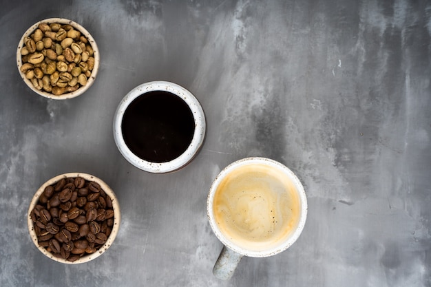 Vier Keramikbecher mit verschiedenen Kaffeestufen. grüne und geröstete Bohnen und Fertiggetränk.