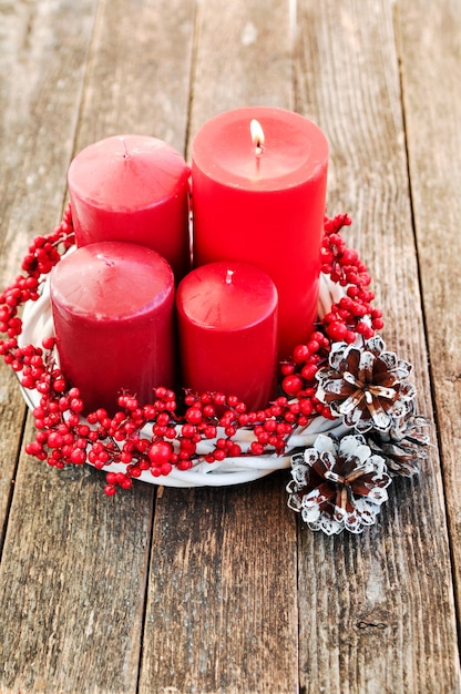 Vier Kerzen in einem weißen Kranz mit roten Beeren auf hölzernem mit Lichtern.