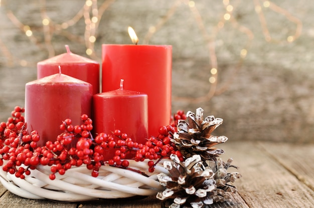 Vier Kerzen in einem weißen Kranz mit roten Beeren auf hölzernem