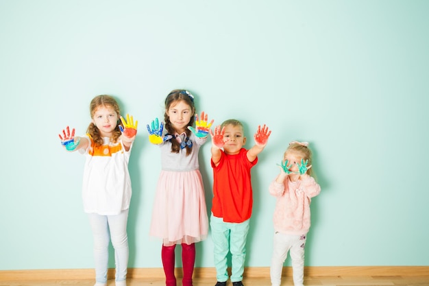 Vier kreative Jungen und Mädchen, die auf dem weißen Hintergrund stehen und ihre bunt bemalten Hände zeigen.