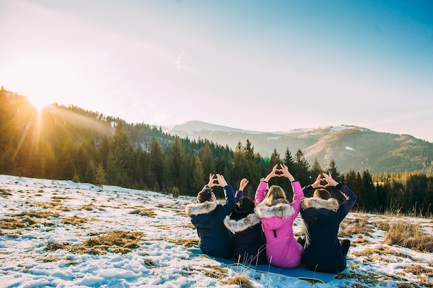 vier Mädchen sitzen im Schnee, sein Rücken zur Kamera, Hände und bilden ein Herz im Winter Berge