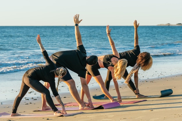 Vier Personen einer Yogastunde strecken sich den Rücken beim Yoga am Strand an einem sonnigen Tag