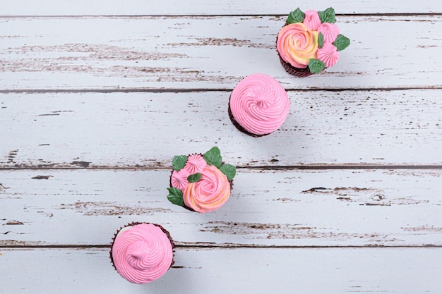 Vier rote Samt-Cupcakes, bedeckt mit rosa Buttercreme. Auf einem weißen Tisch (Draufsicht).