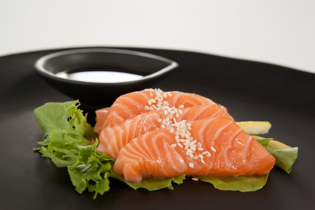 Vier Sashimi-Sushi mit Sojasauce in schwarzer Platte serviert