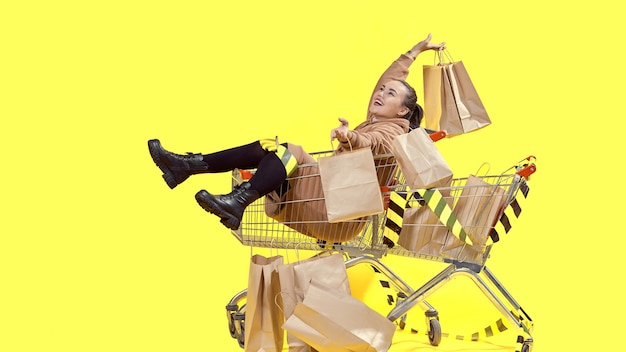 Viernes negro, una niña está sentada en una canasta de compras y riendo, sosteniendo bolsas de compras en sus manos