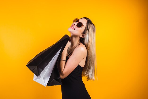Viernes negro - Retrato de mujer joven feliz con bolsas de la compra sobre fondo amarillo.