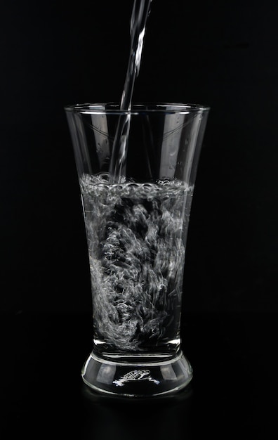 Vierta agua en un vaso aparte sobre un fondo negro