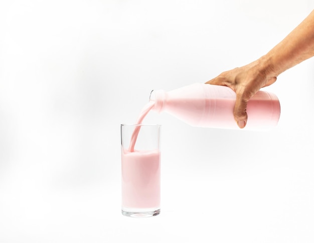 Vierta la leche de fresa de la botella en el vaso Imagen aislada sobre fondo blanco