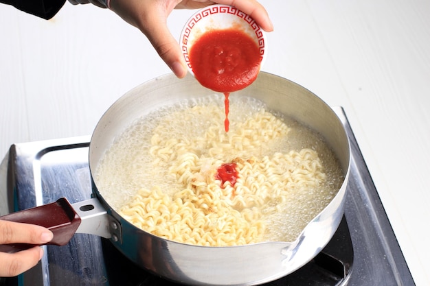 Vierta pasta picante roja al ramyeon coreano instantáneo hervido, proceso de cocción para hacer comida coreana