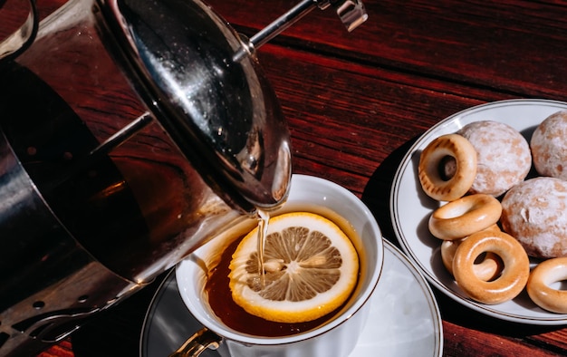 Vierta el té de una tetera en una hermosa taza de cerámica blanca con mango dorado