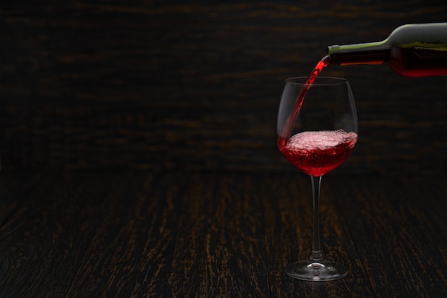 Vierta el vino tinto en un vaso sobre la mesa de madera negra.