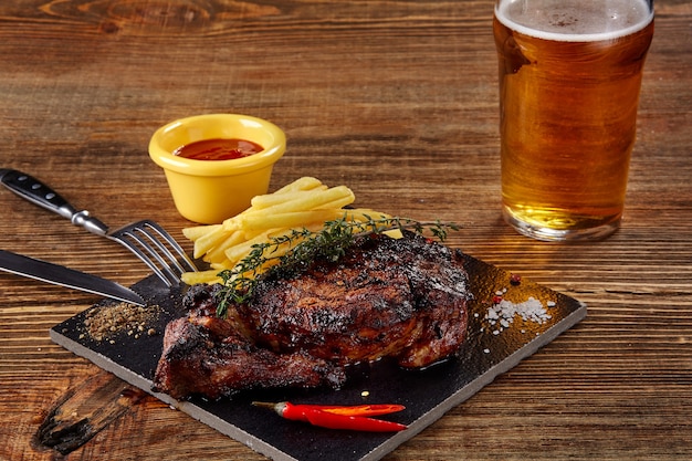 Se vierte la cerveza en un vaso con bistec gourmet y papas fritas sobre fondo de madera